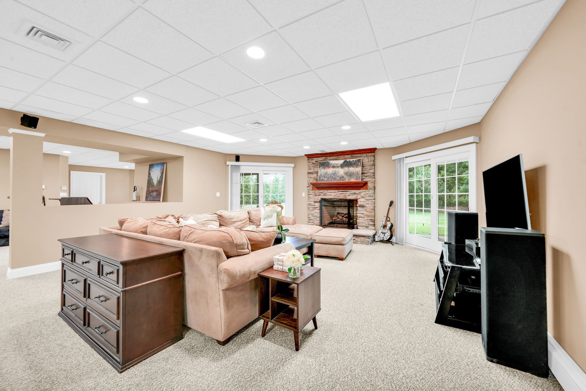 Downstairs, the fully finished and furnished walk-out lower level is built for entertaining, anchored by its own family room warmed by a stone fireplace, oversized windows that flood the space with natural light, French doors leading to a covered patio and the flat, grassy backyard beyond, and its own separate entrance from the garage in addition to access from the main living areas.