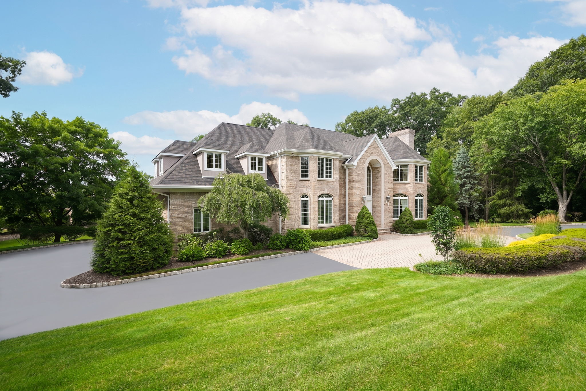 The approach alone tells you what you're in for. A circular driveway, anchored by a paver walkway at its center, sweeps past manicured grounds toward an oversized three-car garage and an entrance built for arrival, framed by brick on three sides of the home's exterior.