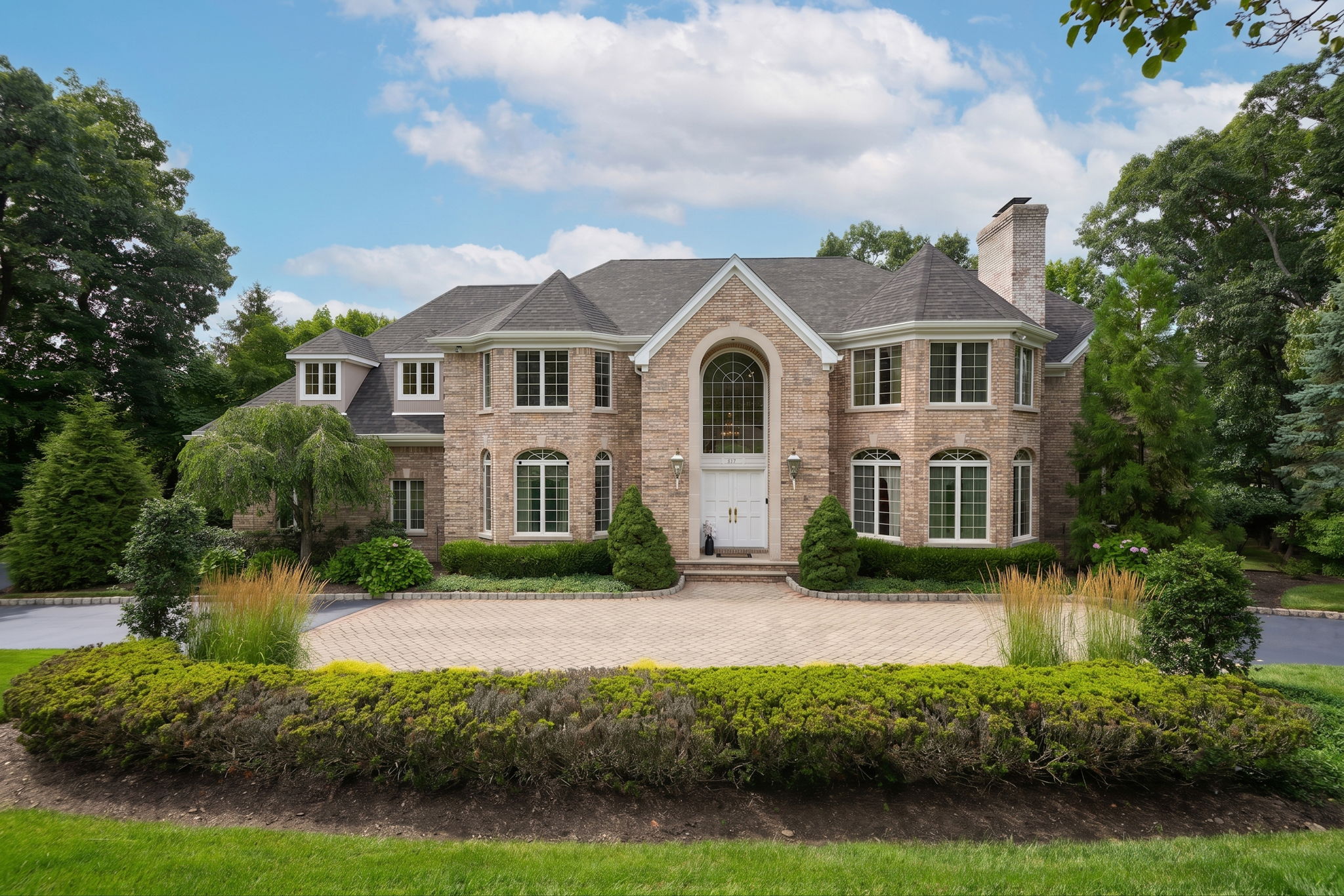 The approach alone tells you what you're in for. A circular driveway, anchored by a paver walkway at its center, sweeps past manicured grounds toward an oversized three-car garage and an entrance built for arrival, framed by brick on three sides of the home's exterior.
