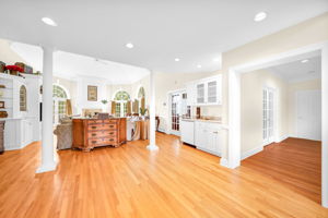 The great room itself is a showstopper: a soaring, two-story space beneath a dramatic vaulted ceiling with a graceful ceiling fan and elegant wall paneling throughout. A fireplace framed in detailed white millwork anchors the room, flanked by arched, palladian-style windows dressed in rich gold drapery, while double French doors open onto an expansive back deck and the flat, grassy backyard beyond. Rich hardwood floors and built-in cabinetry complete a space made for both grand entertaining and quiet evenings in.