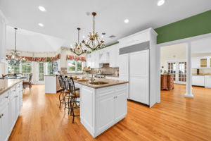 To the left, the kitchen: a bright, all-white showpiece with a large island for prepping or casual dining, an eat-in nook for everyday meals, a walk-in pantry, and a butler's pantry connecting seamlessly to the formal dining room. And just off the kitchen, in a detail only a homeowner who truly lived in the space would think to include, a second staircase with a wooden ladder rail, scaled for little hands and big hands alike, is tucked charmingly beside the everyday comings and goings of family life.