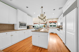 To the left, the kitchen: a bright, all-white showpiece with a large island for prepping or casual dining, an eat-in nook for everyday meals, a walk-in pantry, and a butler's pantry connecting seamlessly to the formal dining room. And just off the kitchen, in a detail only a homeowner who truly lived in the space would think to include, a second staircase with a wooden ladder rail, scaled for little hands and big hands alike, is tucked charmingly beside the everyday comings and goings of family life.