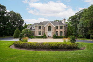 The approach alone tells you what you're in for. A circular driveway, anchored by a paver walkway at its center, sweeps past manicured grounds toward an oversized three-car garage and an entrance built for arrival, framed by brick on three sides of the home's exterior.