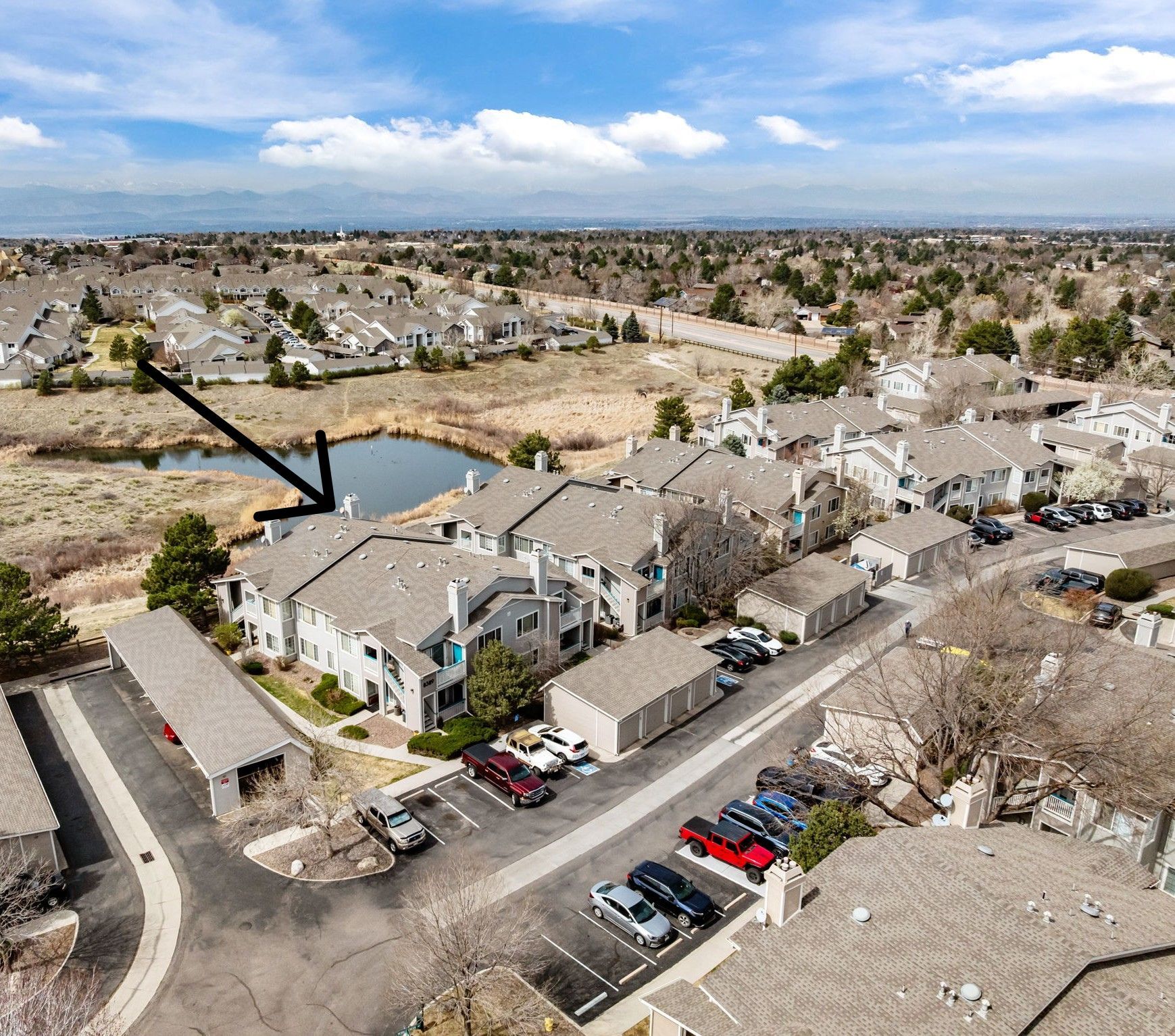 Aerial view of condo building, pond, open space and panoramic view of mountains peeking out from behind the clouds