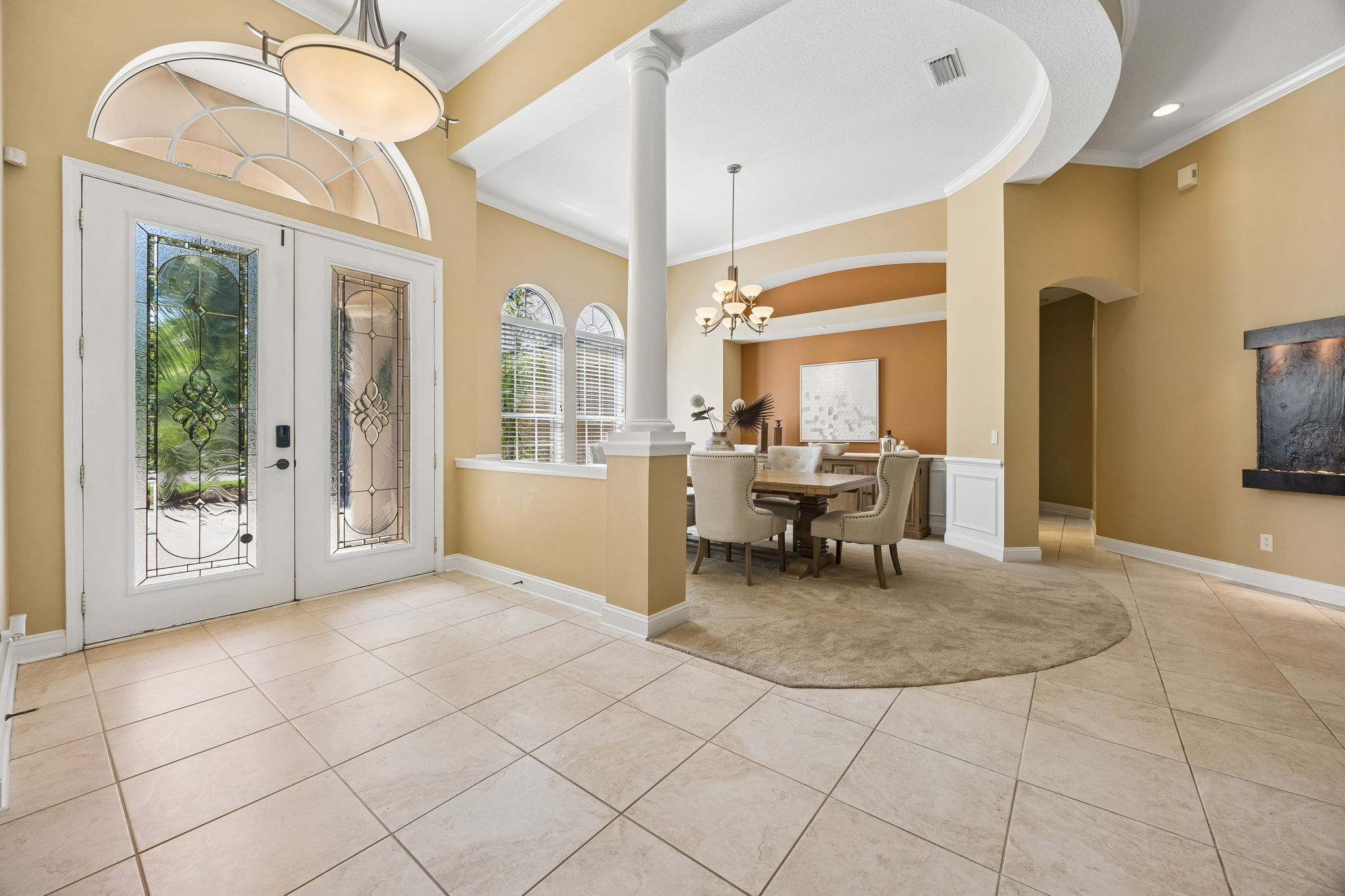 A gracious entry introduces the home with arched glass, columns, and a formal dining room just beyond ...