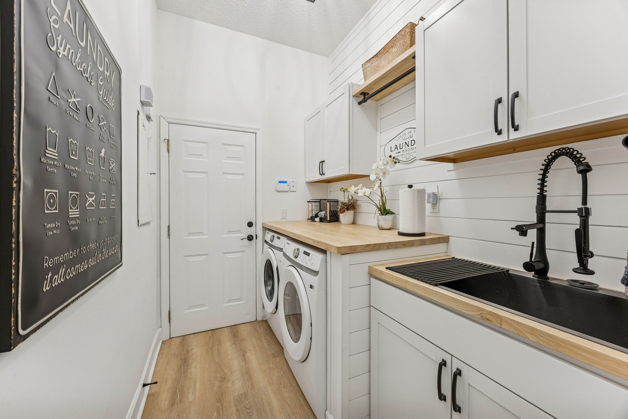 Even the laundry room is beautifully finished, featuring custom cabinetry, warm wood countertops, and a matte black utility sink