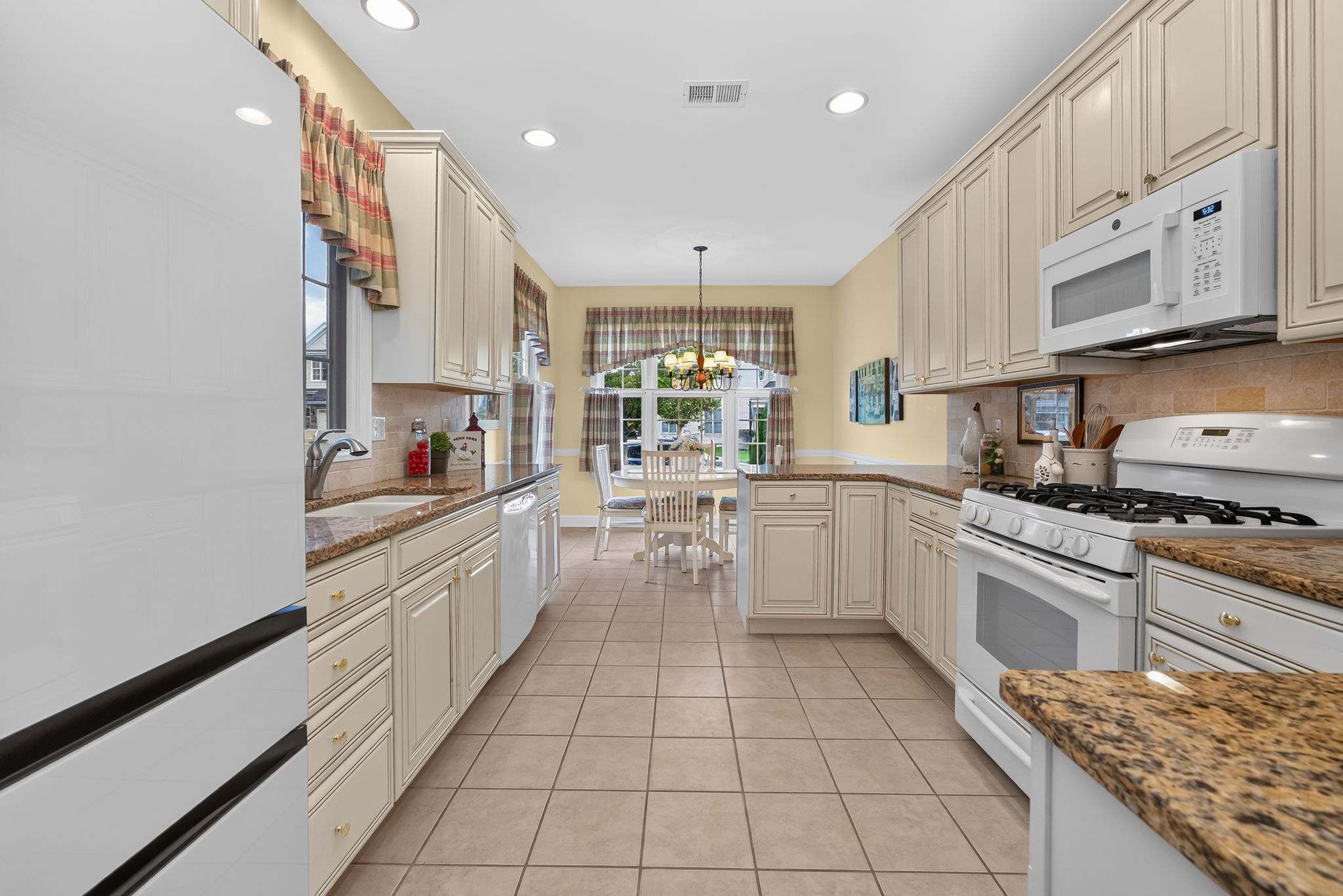 The eat-in kitchen is appointed with upgraded cabinetry, 42-inch upper cabinets, granite countertops, a tum-bled tile backsplash, and quality appliances.