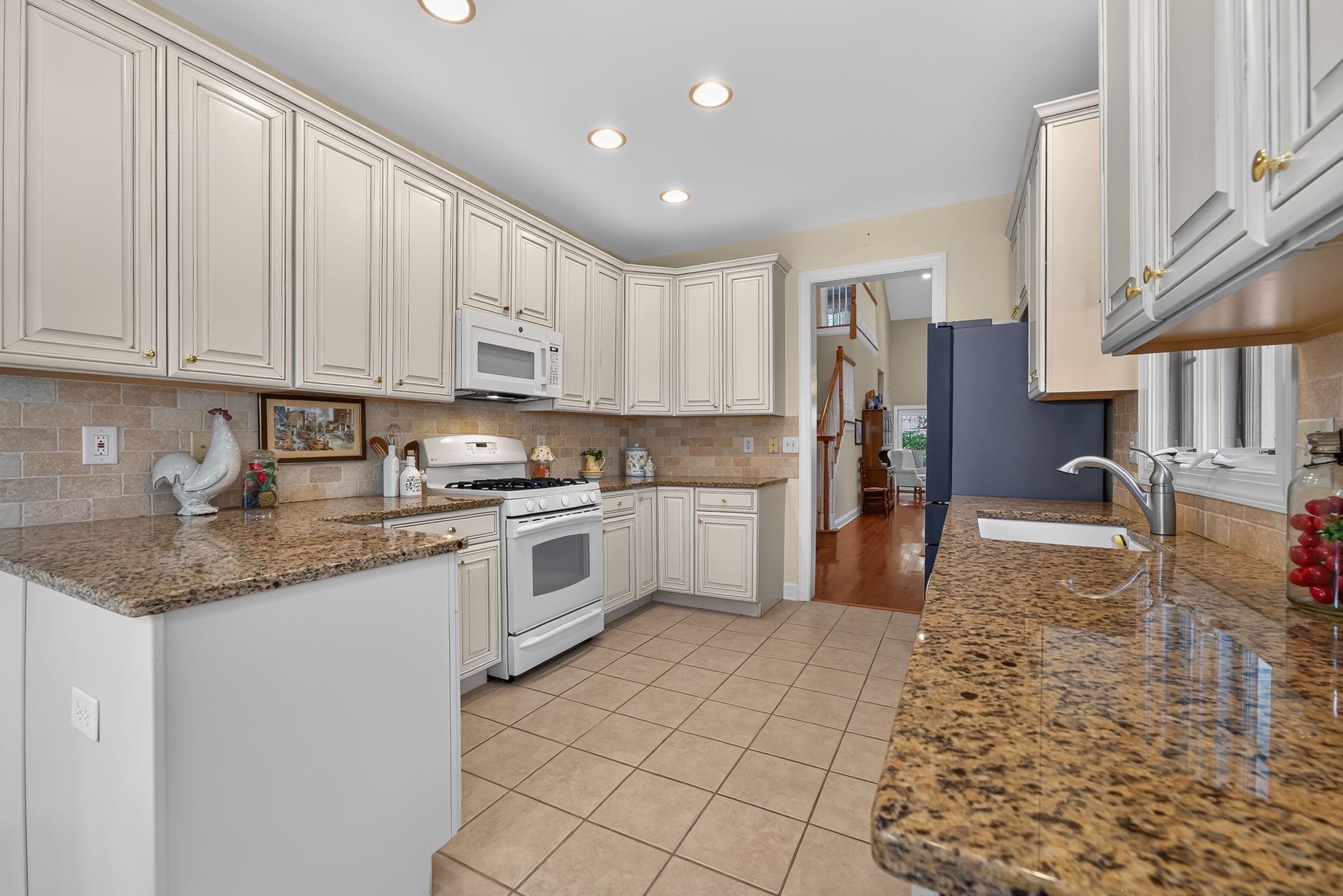 The eat-in kitchen is appointed with upgraded cabinetry, 42-inch upper cabinets, granite countertops, a tum-bled tile backsplash, and quality appliances.