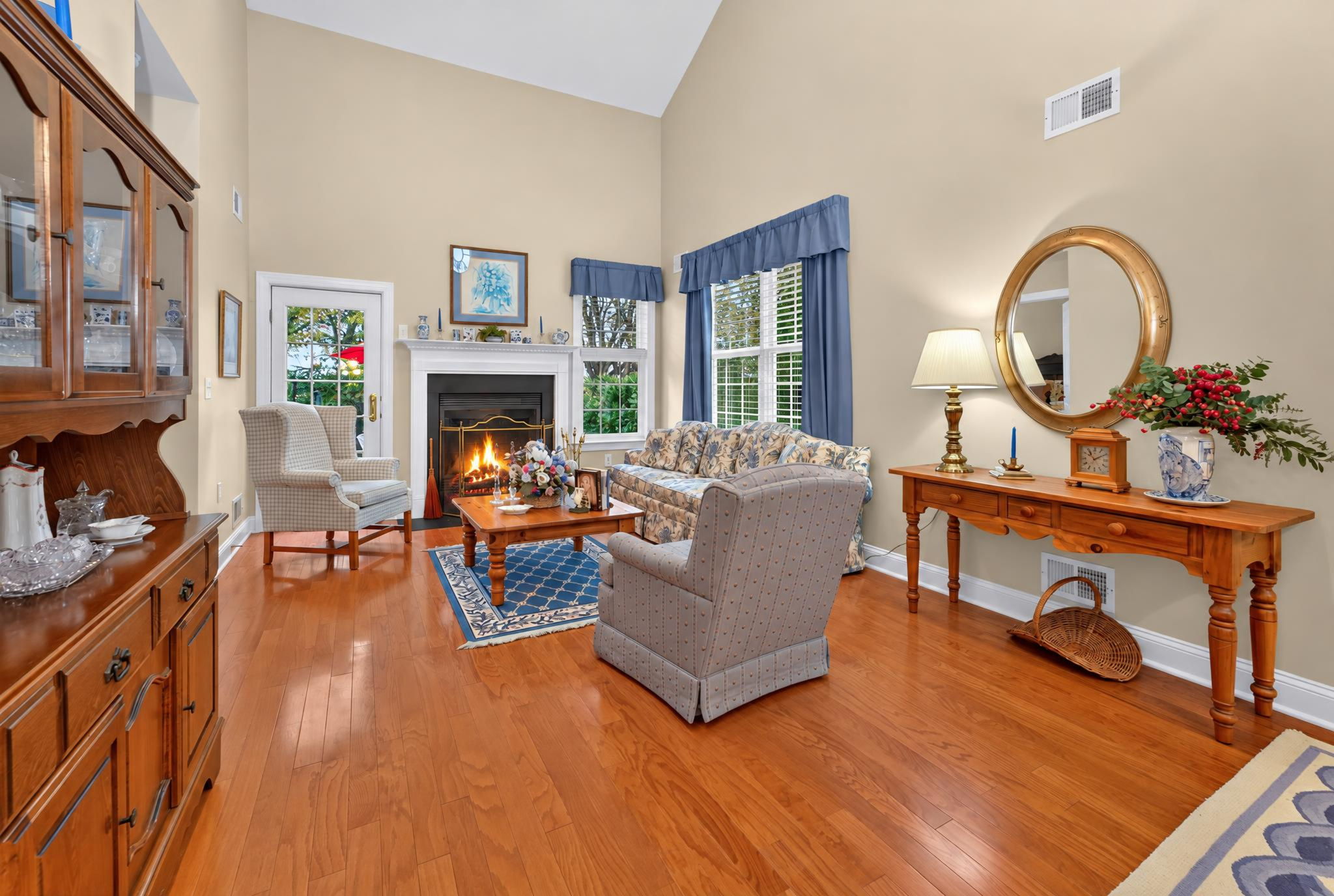 TWO STORY LIVING ROOM A French door opens to a paver patio overlooking a peaceful backdrop of mature trees and open green space.