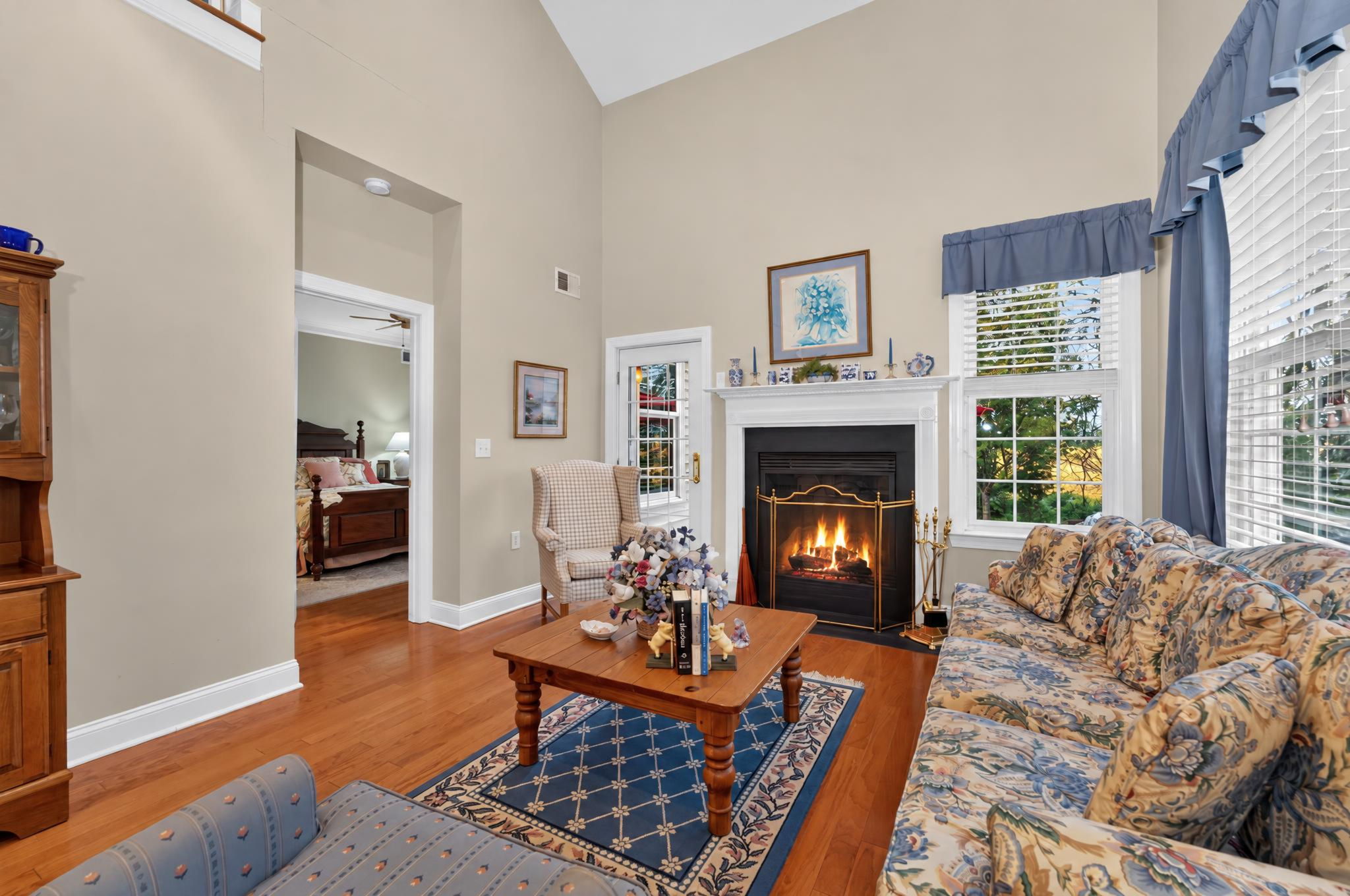 TWO STORY LIVING ROOM A French door opens to a paver patio overlooking a peaceful backdrop of mature trees and open green space.