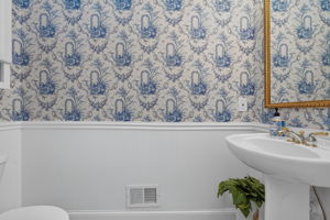 HALF BATH The half bath features a mini chandelier, pedestal sink, chair rail moulding, and hardwood flooring.