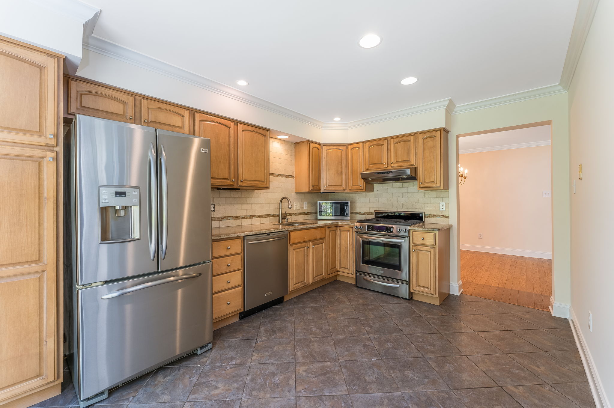 The renovated kitchen features raised-panel cabinetry with soft close drawers and pantry, granite counter tops, ceramic tile backsplash, stainless steel appliances, and ceramic tile floor.
