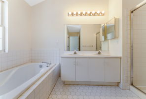 The en suite bath offers a high ceiling, double basins in white vanity, soaking tub and shower in tile surround, ceramic tile floor.