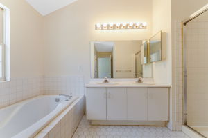 The en suite bath offers a high ceiling, double basins in white vanity, soaking tub and shower in tile surround, ceramic tile floor.