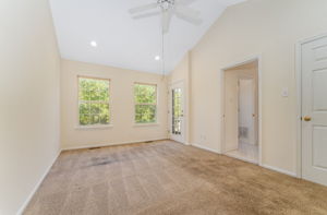 The primary bedroom features a cathedral ceiling, recessed lighting, ceiling fan, walk-in closet, and neutral carpeting, with direct access to a private deck.