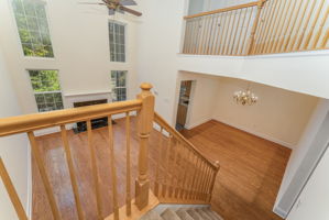 A turned staircase leads to an open balcony with full view of the great room below. Other features include an iron chandelier and carpeted steps and landing.