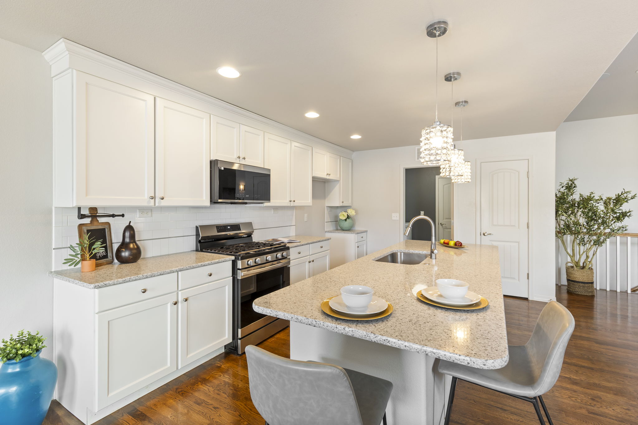 Kitchen with stainless steel appliances, light stone countertops, a kitchen breakfast bar, white cabinets, and hardwood floors