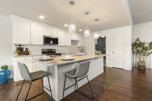 Kitchen with stone countertops, large center island with seating, white cabinetry, and pendant lighting.