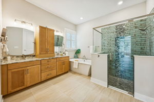 The beautifully appointed primary bath features warm maple-toned cabinetry ...