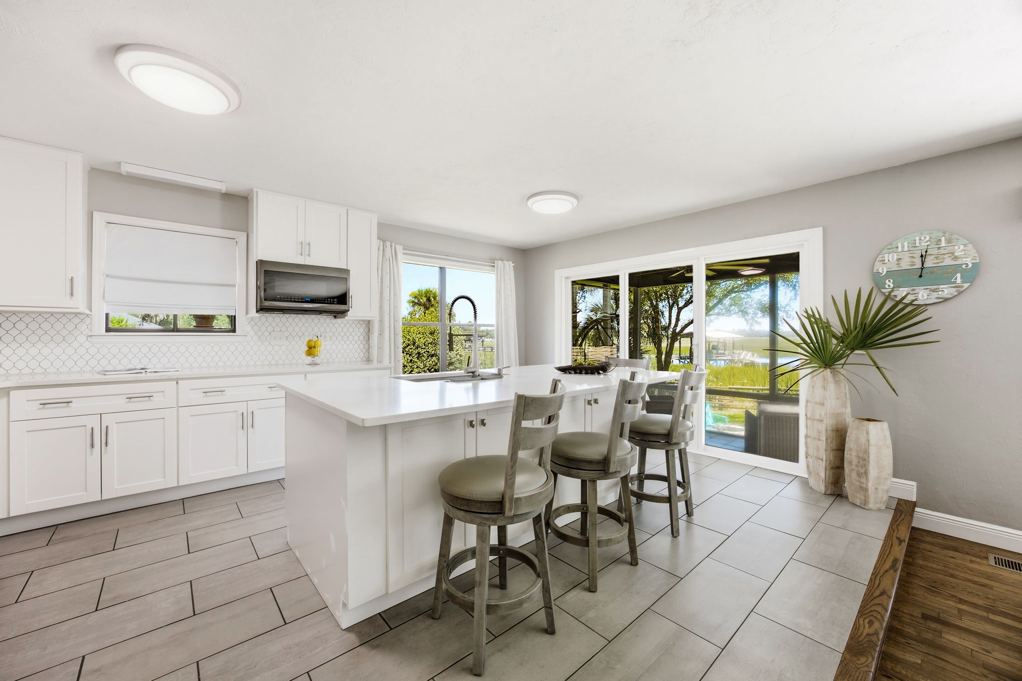 The renovated kitchen begins with a generous island, crisp finishes and waterfront views beyond the screened porch