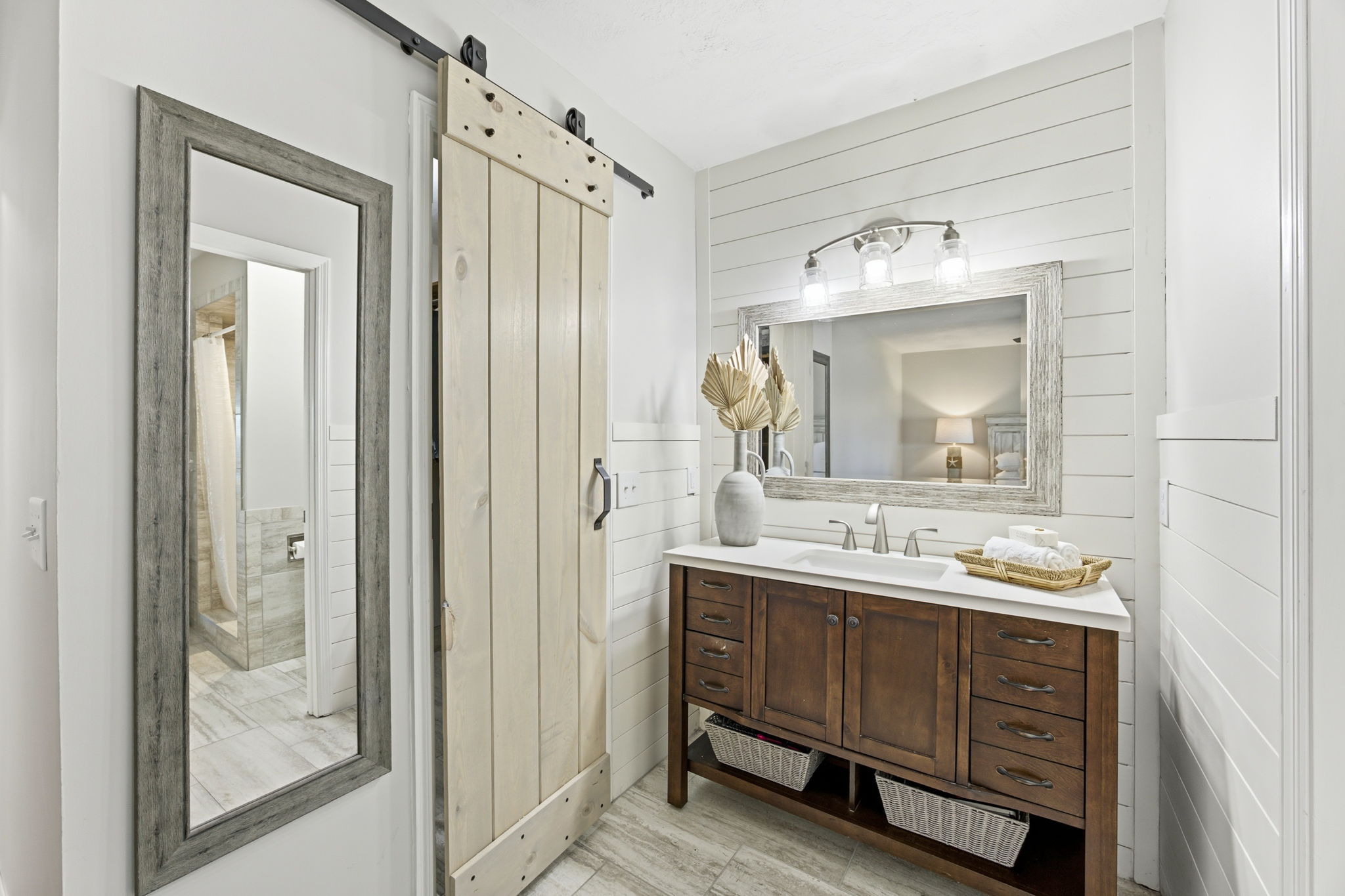 The renovated primary bath begins with shiplap walls, a warm wood vanity and a softly weathered coastal palette