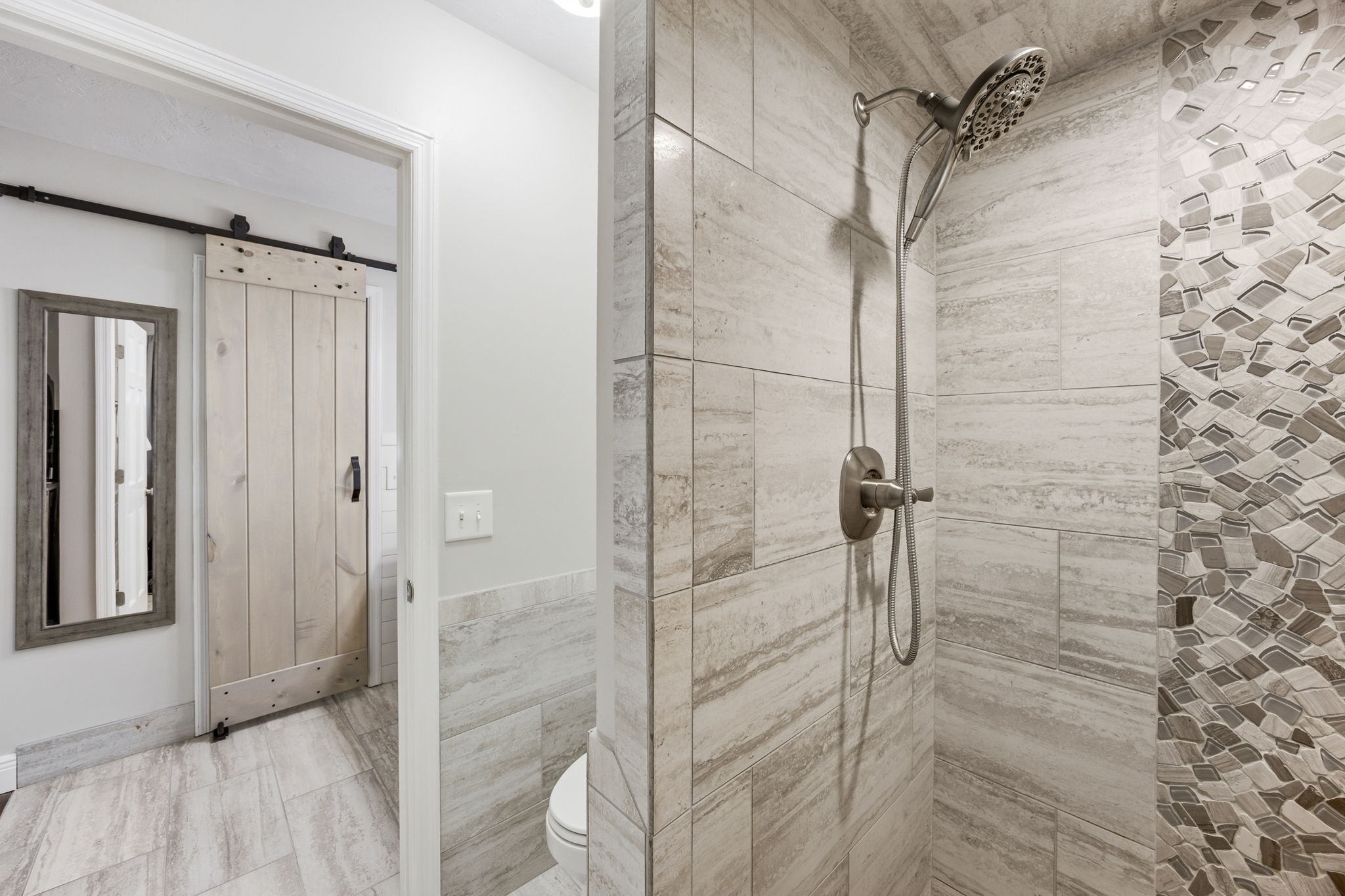 A tiled walk-in shower adds texture and function, finished with a handheld shower and decorative accent wall