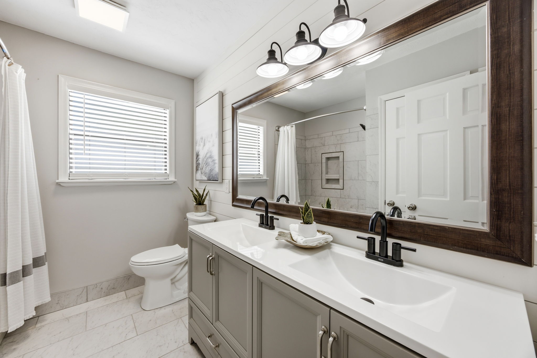 The renovated guest bath pairs a double vanity with shiplap detail, crisp finishes and thoughtful storage