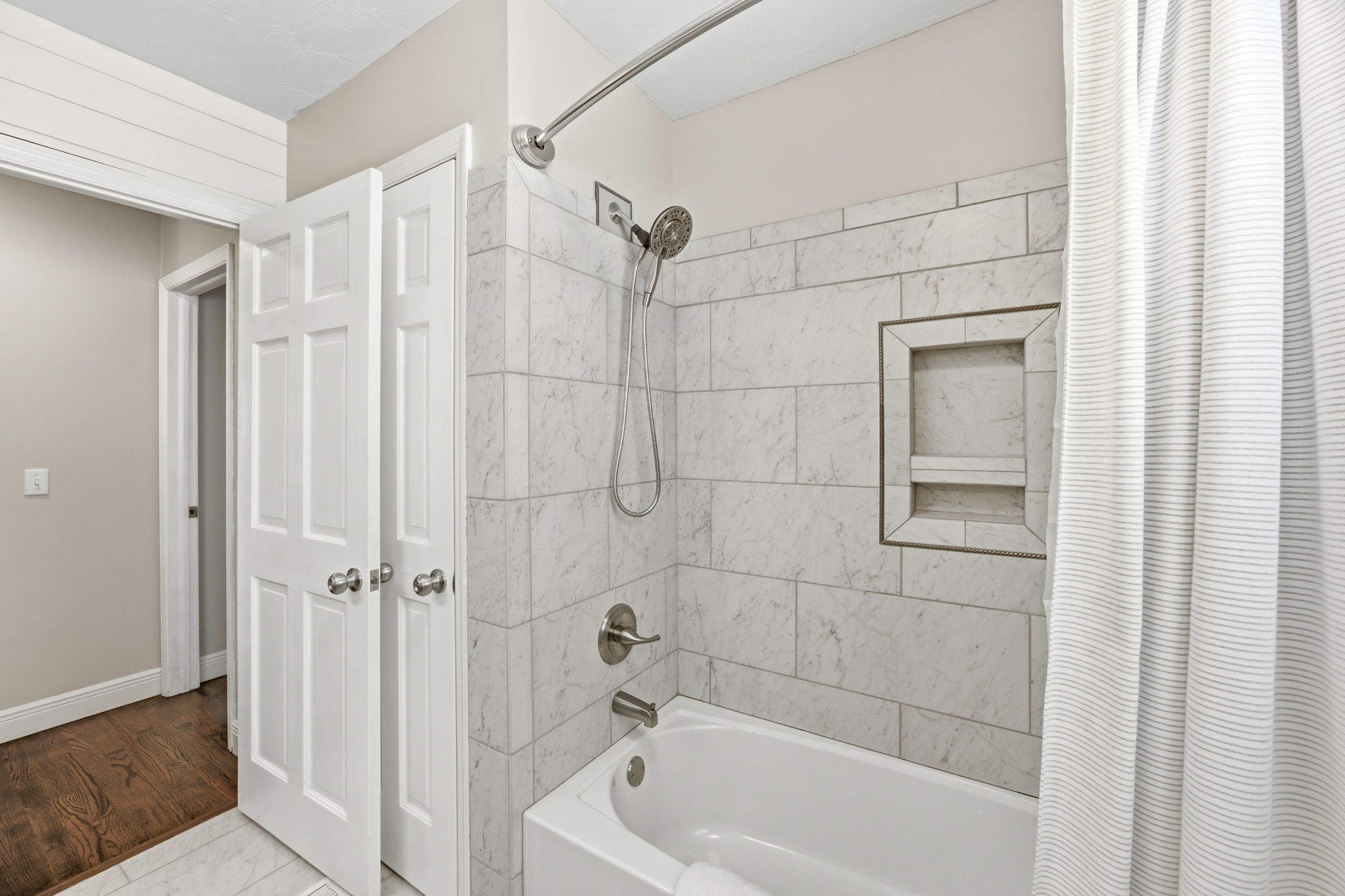 A tiled tub and shower surround completes the bath with a clean, polished finish and practical built-in niche