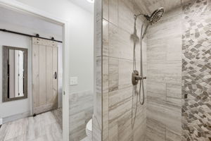 A tiled walk-in shower adds texture and function, finished with a handheld shower and decorative accent wall