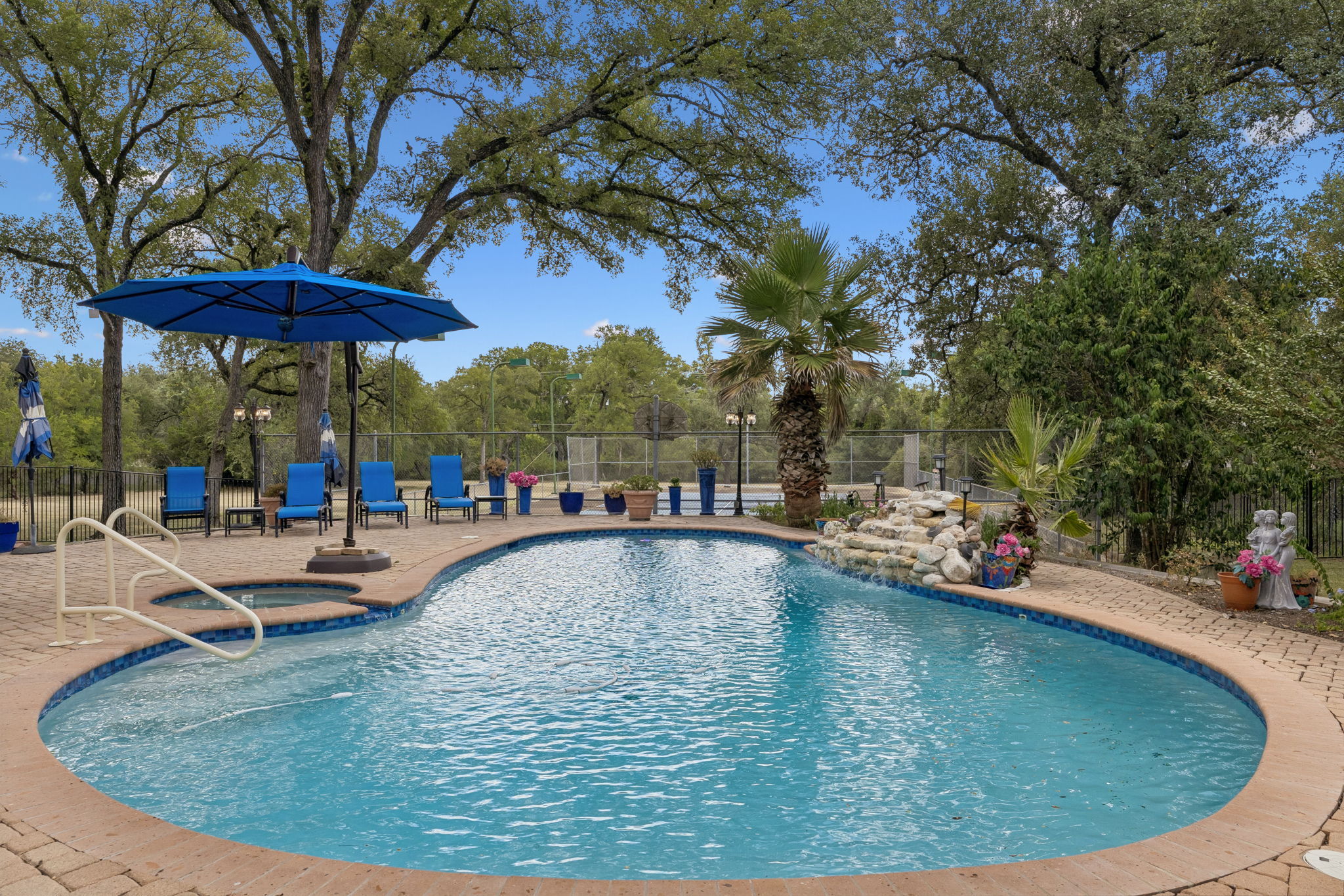 An inviting backyard oasis awaits with a sparkling pool and spa, set on a paver patio amidst mature trees.