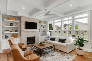 Family room with coffered ceilings, built in cabinets, floating shelfs, ceiling speakers with Sonos system, and gas fireplace with brick surround